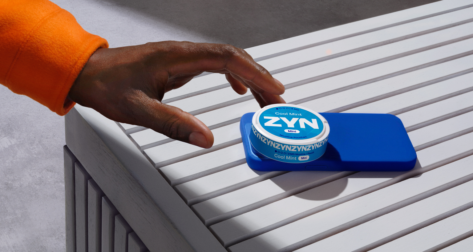 Hand reaching out to a light blue ZYN nicotine pouch can